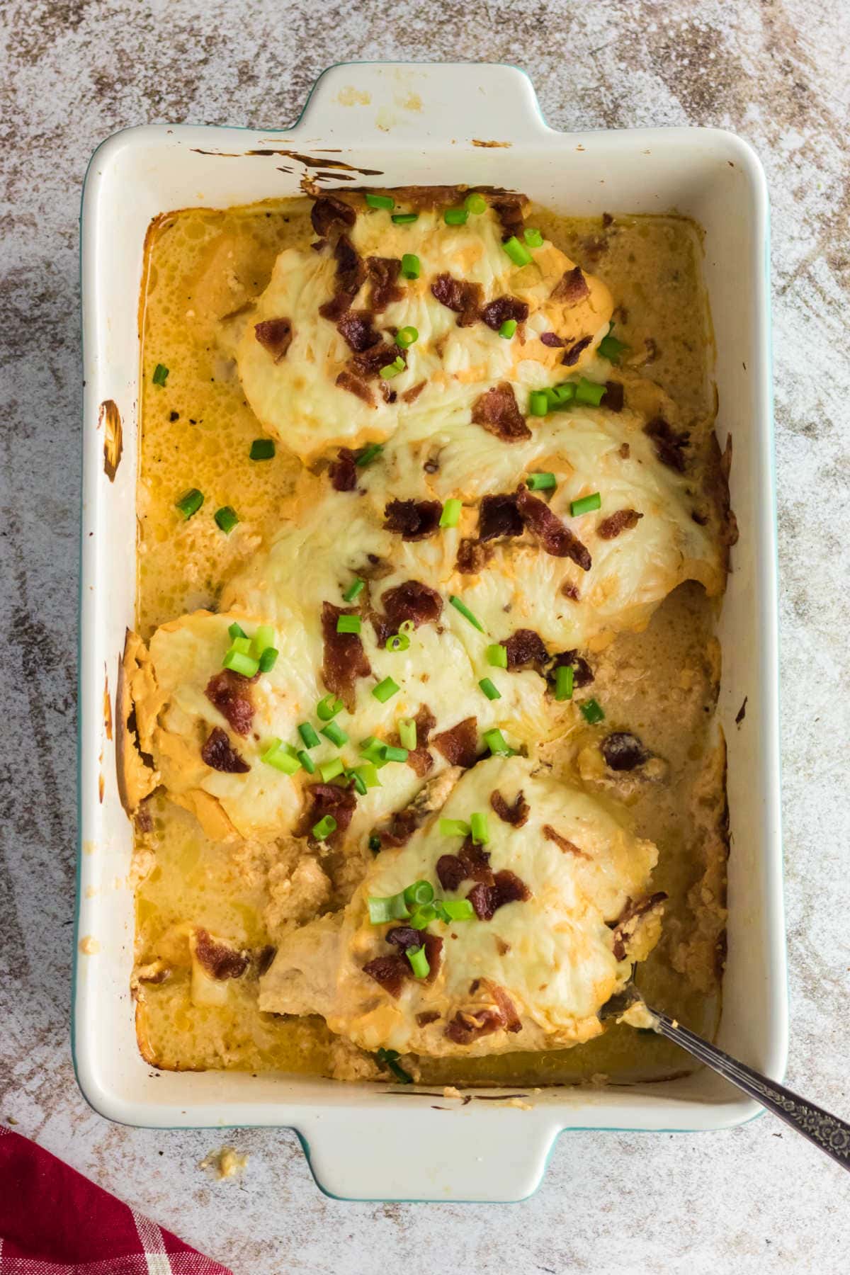 Overhead view of baked chicken breast in a sauce garnished with bacon and green onions.