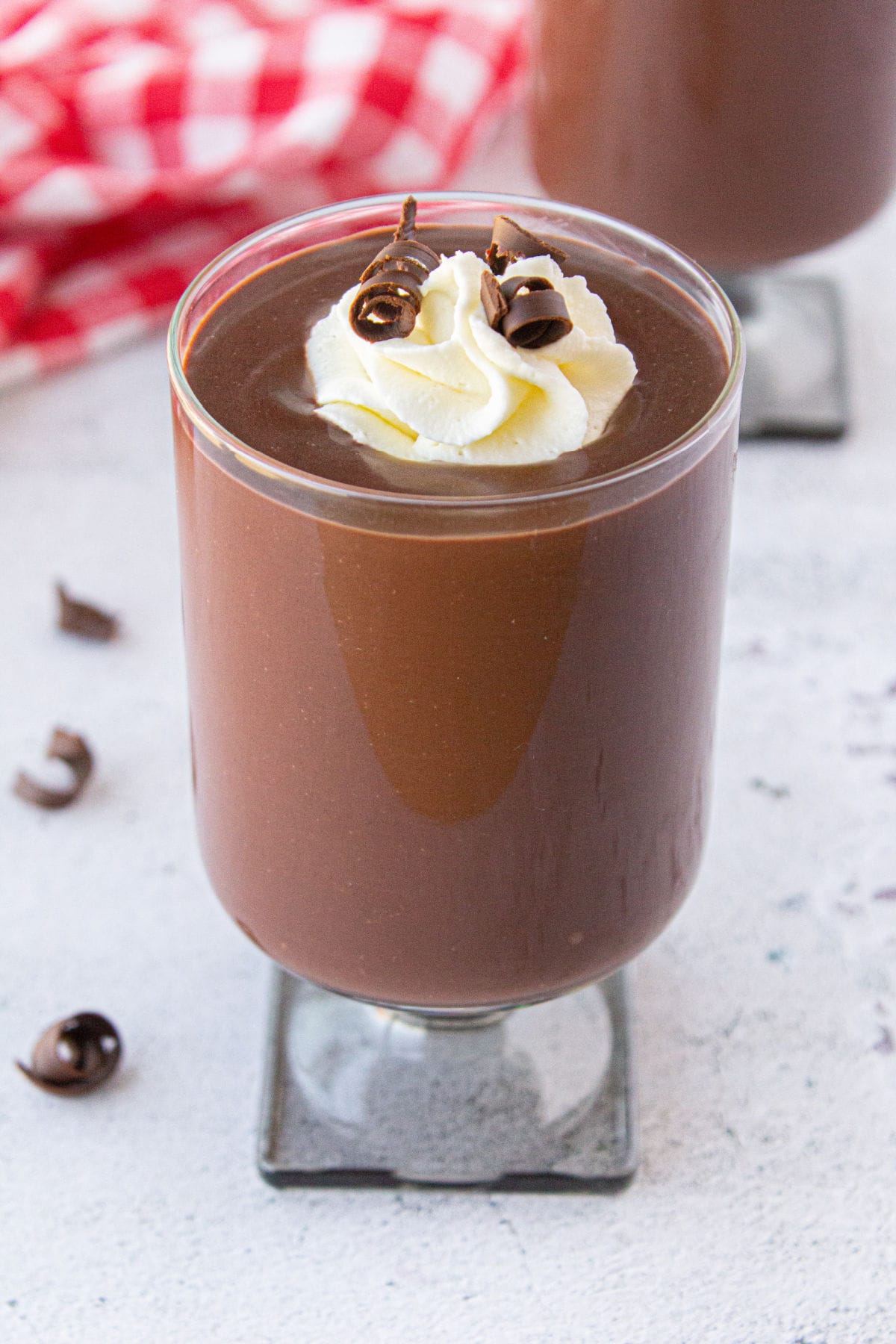 A closeup of a glass filled with pudding and topped with whipped cream and chocolate curls.