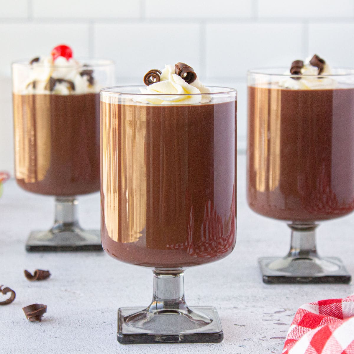 Three glasses filled with chocolate pudding on a white table.