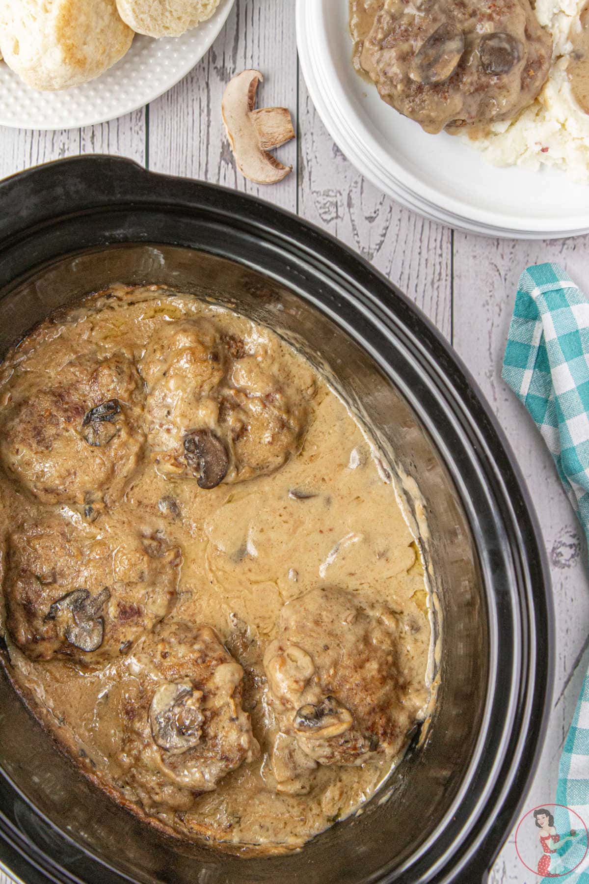 A crockpot with hamburger steaks, mushrooms, and gravy in it.