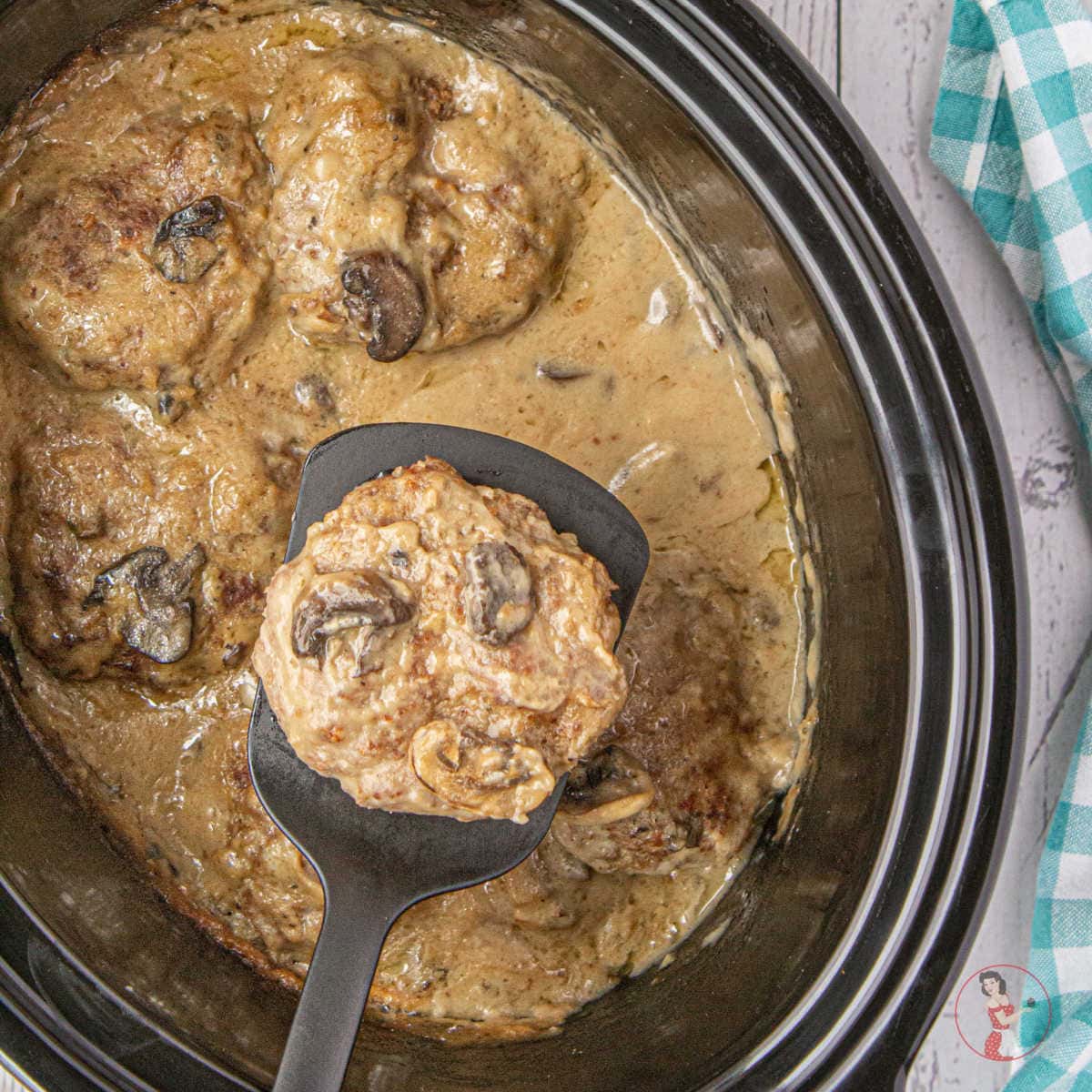 A serving of salisbury steak being lifted from a slow cooker.