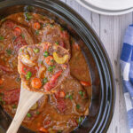 A ladle filled with a serving of swiss steak.