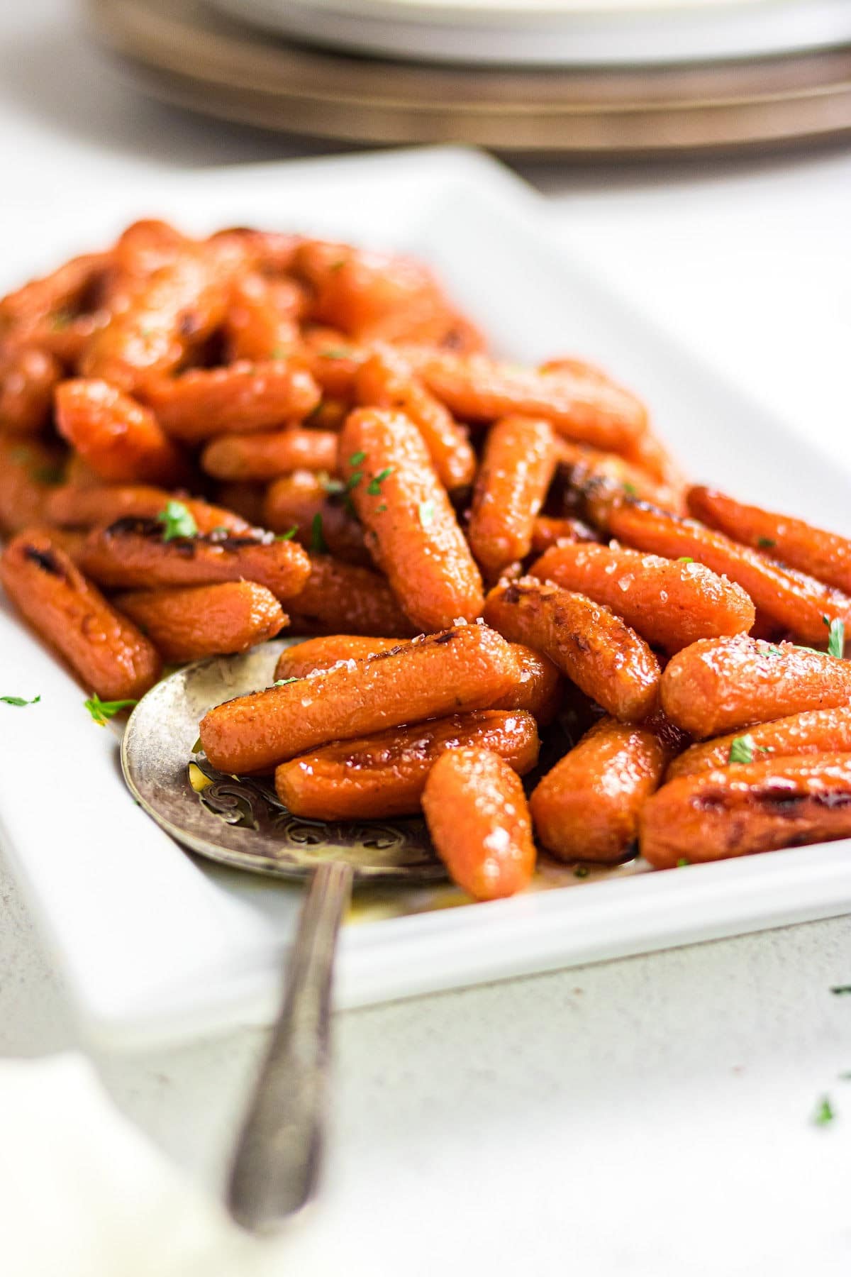 A serving platter stacked with baby carrots that have been glazed and roasted.