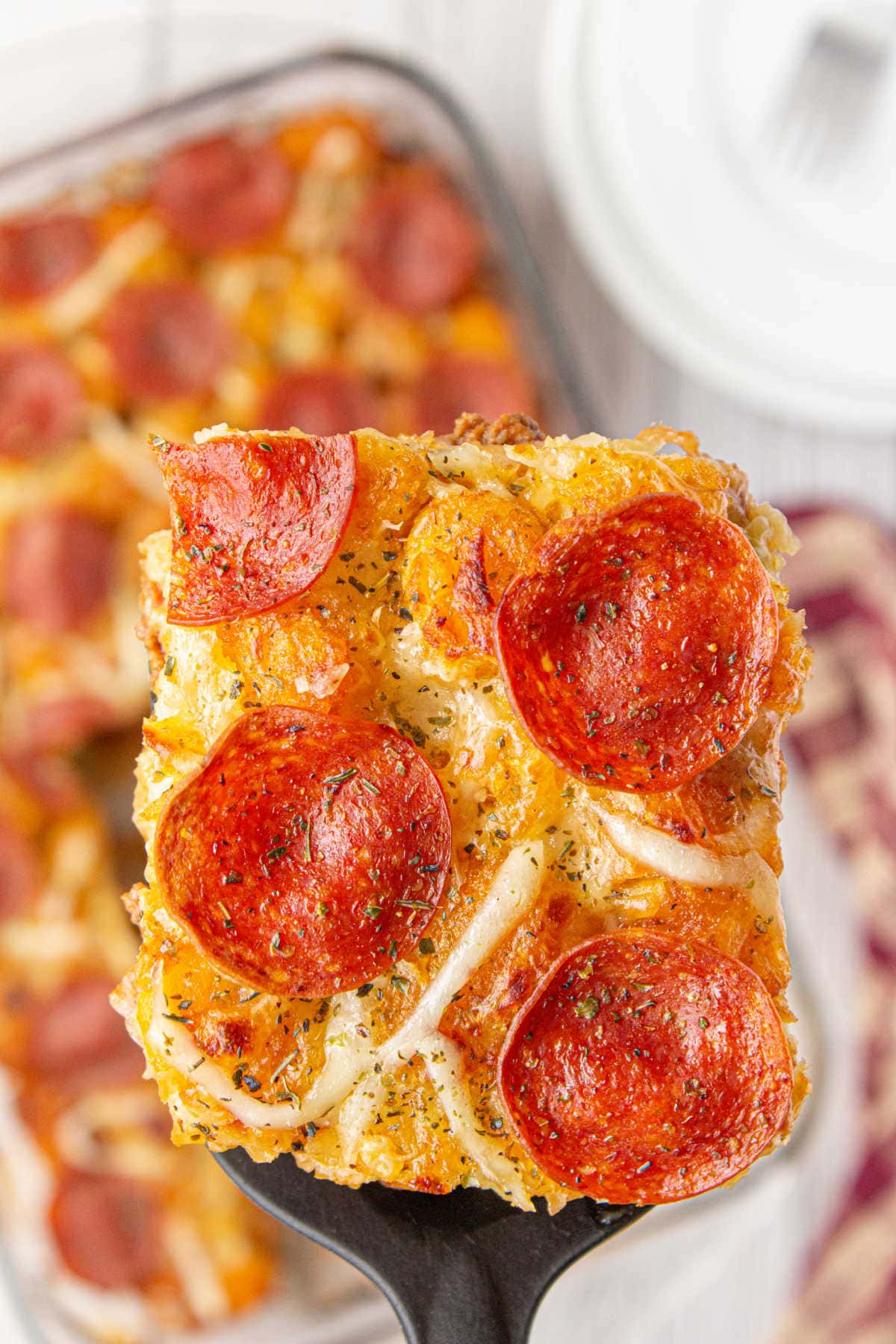 A serving of pizza tater tot casserole being removed from the dish.