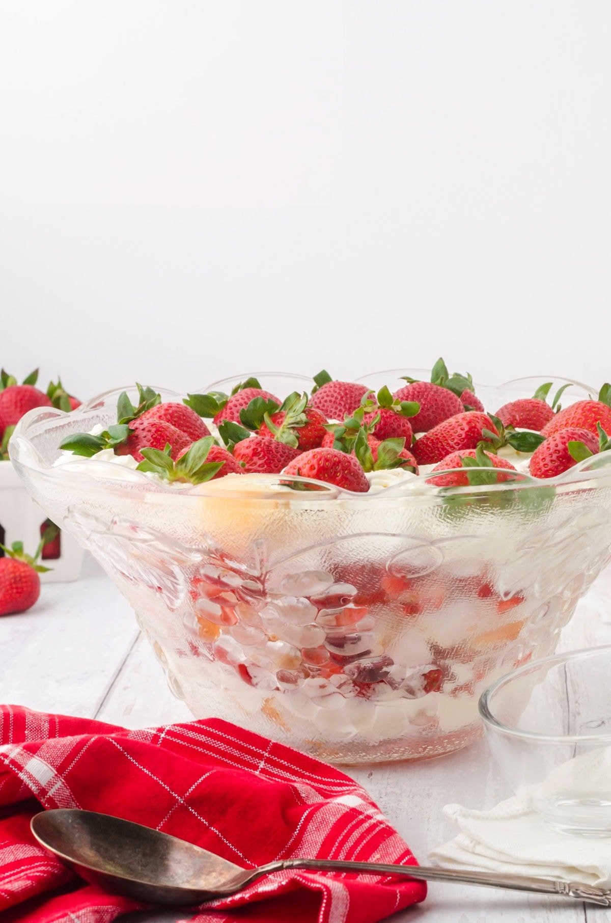 Side view of a glass punch bowl filled with layers of strawberries, whipped cream, and cake.