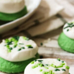 Green cookies with thick, white buttercream frosting on top.
