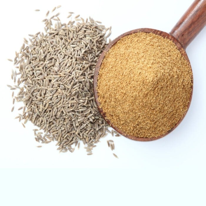 A pile of cumin seed next to a spoonful of ground cumin.