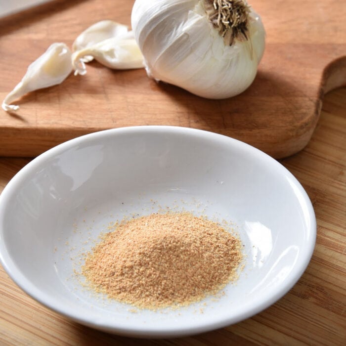 A bowl of ground garlic with a garlic clove in the background.