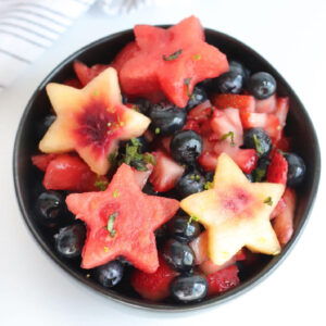 Overhead view of a bowl of red, white, and blue fruit cut in star shapes.