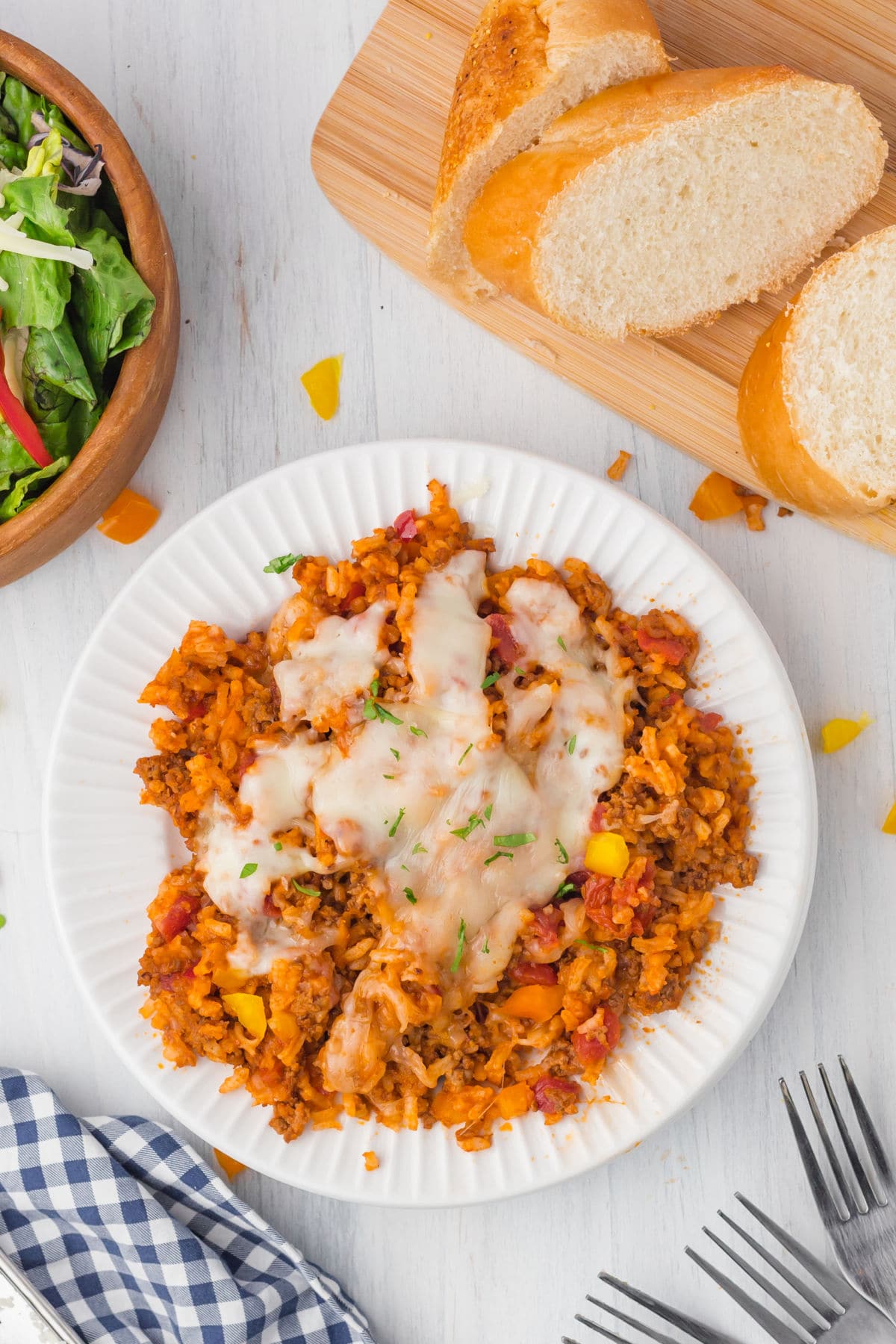 Delicious ground beef and rice casserole served up on a white plate with slices of bread and a salad.