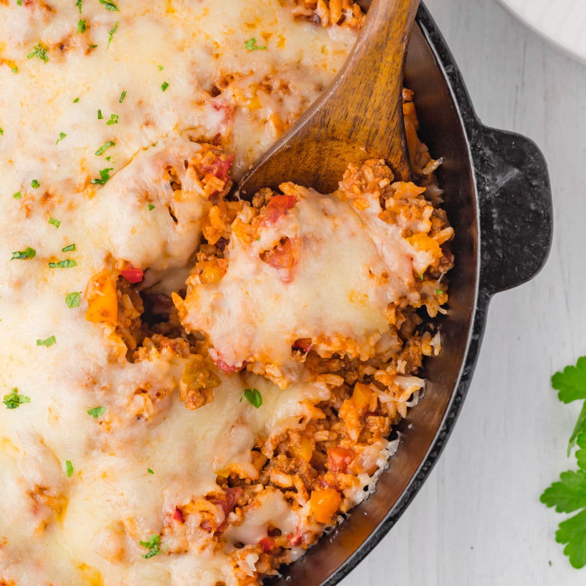 Closeup of ground beef . tomatoes, peppers, and rice casserole in an iron skillet with a wooden spoon.