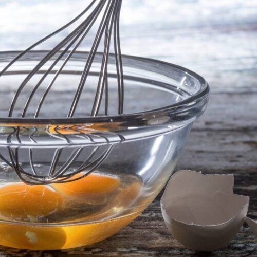 A balloon whisk in a glass bowl with egg yolks,