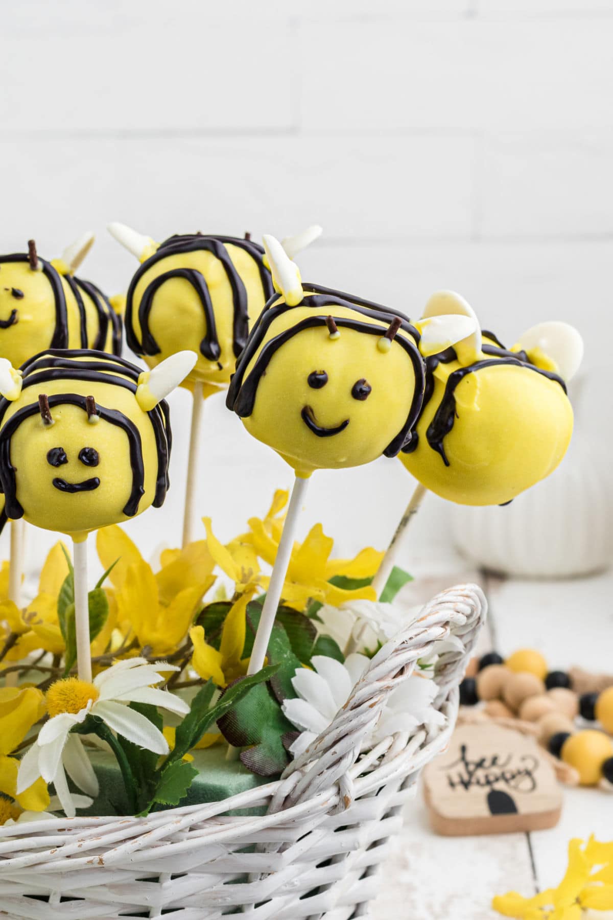 Several finished bumble bee cake pops standing up in a basket of flowers.