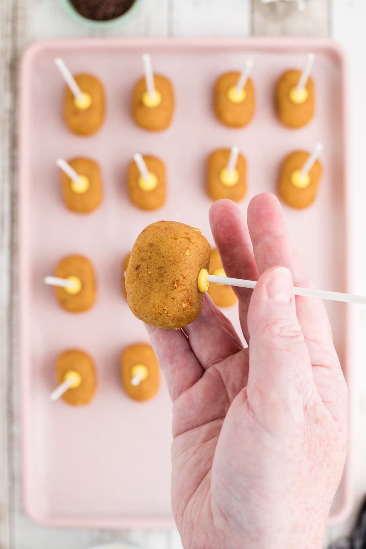 Showing how to insert the stick into the cake pop and secure with a dab of melted candy.