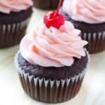 Chocolate cupcake with pink frosting and a cherry on top.