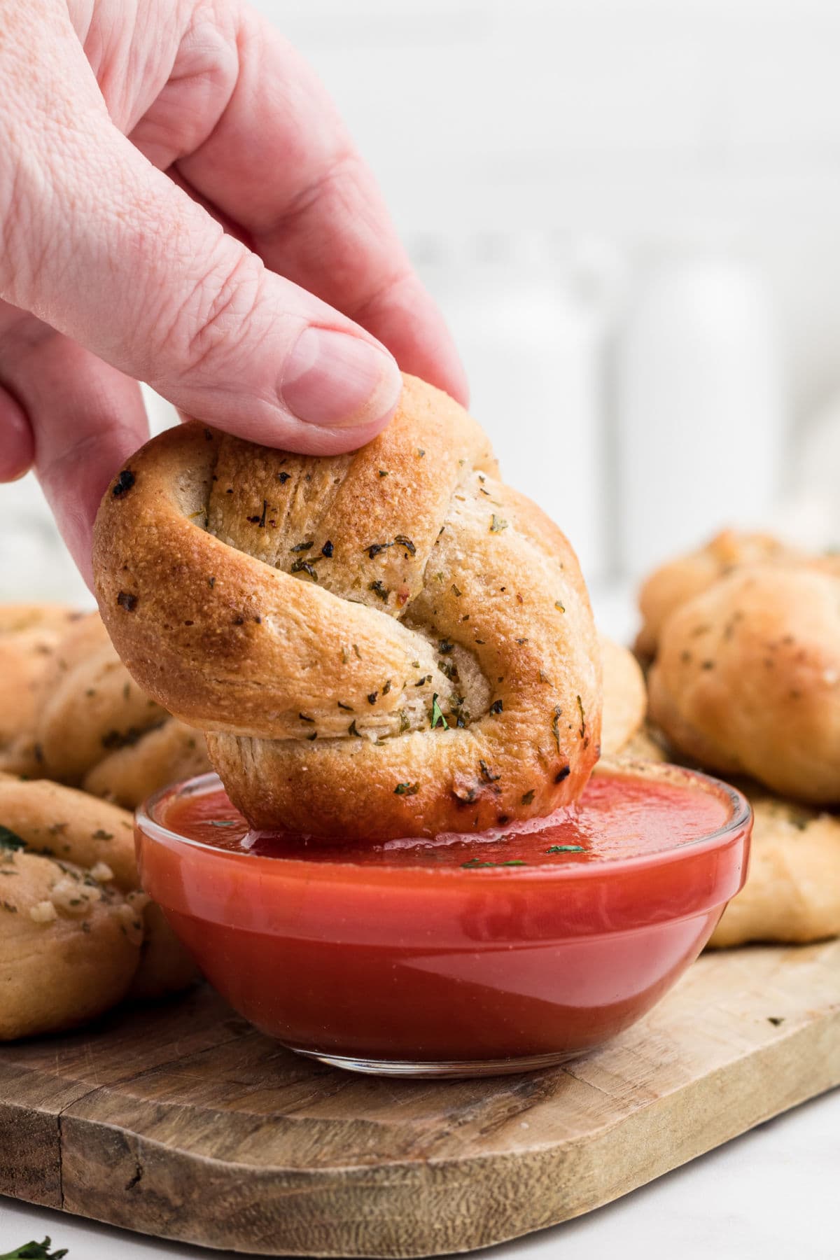A hand dipping a roll into red marinara sauce.
