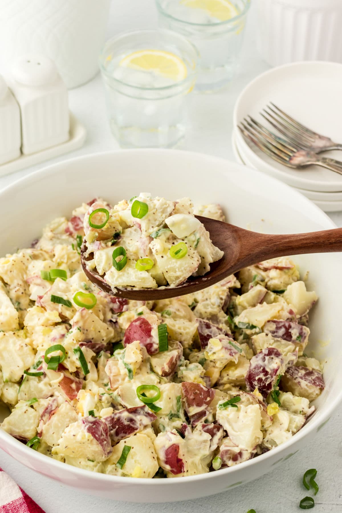 A serving bowl of potato salad with a serving spoon.