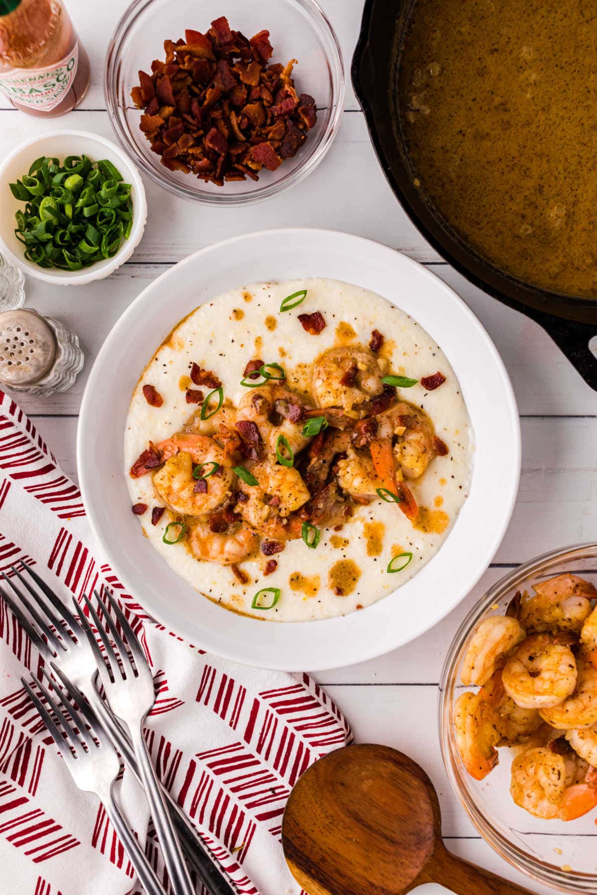 Overhead view of a bowl of shrimp and grits being garnished with green onions and bacon.