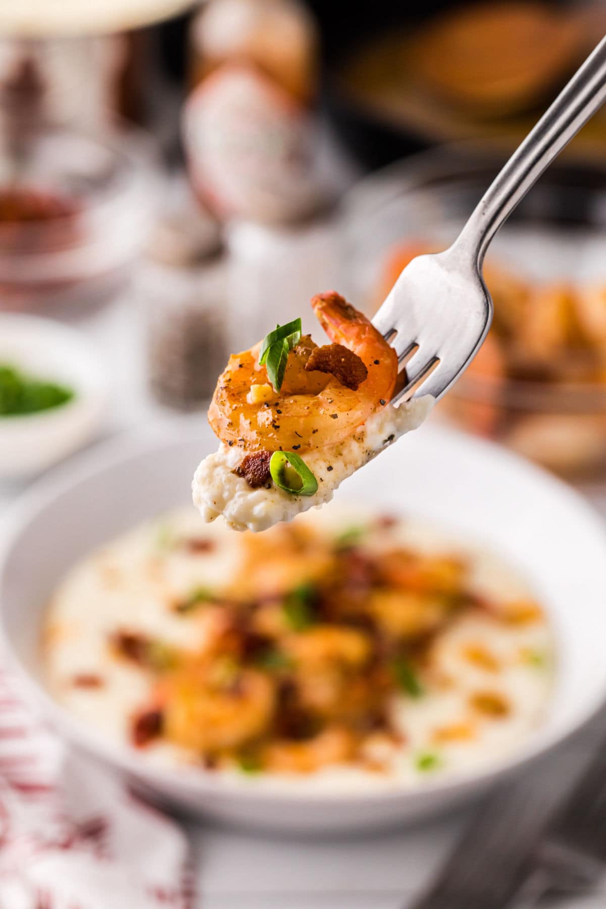 A fork lifting a bite of shrimp and grits from a bowl