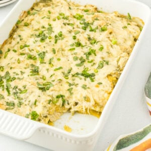 Closeup of the casserole in a dish with a serving removed to show the layers of tortillas, chicken, and cheese.