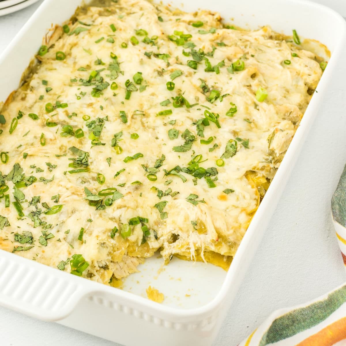 Closeup of the casserole in a dish with a serving removed to show the layers of tortillas, chicken, and cheese.