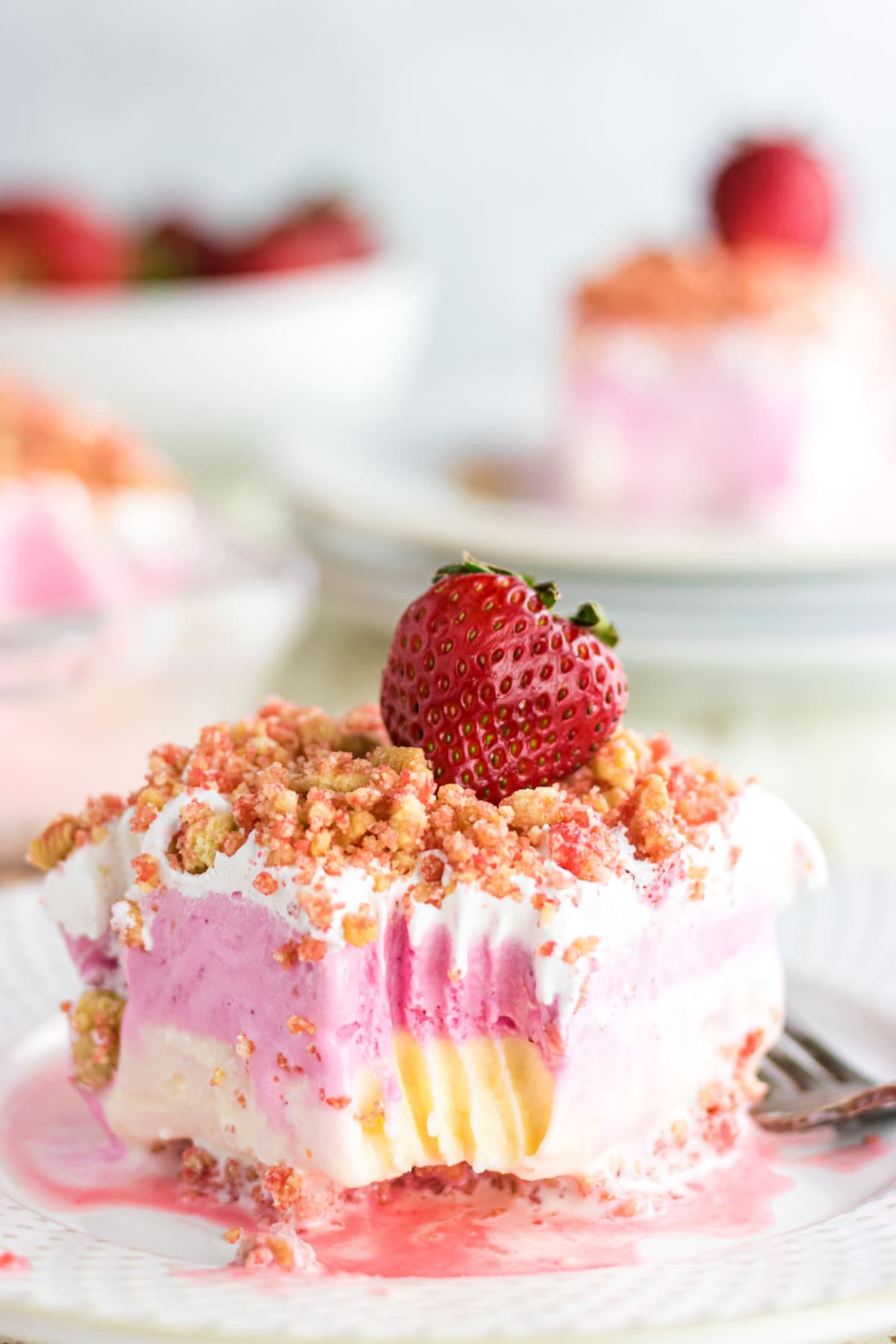 A closeup of a slice of strawberry crunch ice cream cake with a strawberry on top.