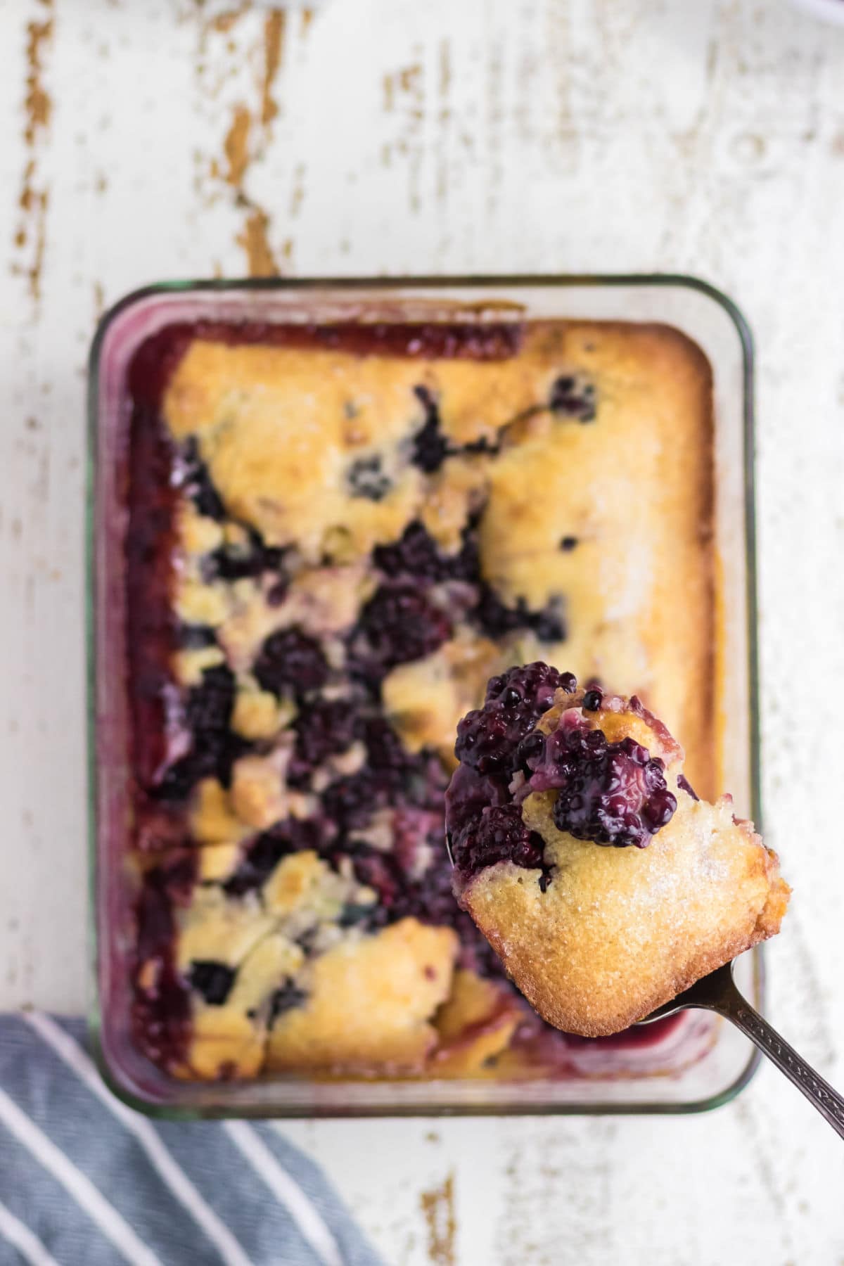 A serving of blackberry cobbler is being removed from the pan.