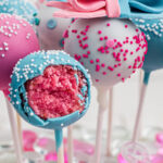 Closeup of the cake pops with a blue one opened to see the pink cake inside. Title text overlay for Pinterest.