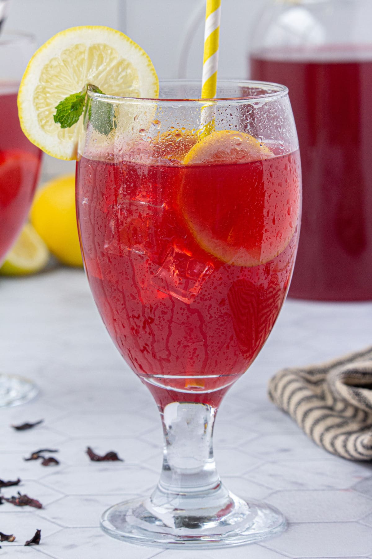 A glass of bright red hibiscus lemonade with a yellow and white straw.
