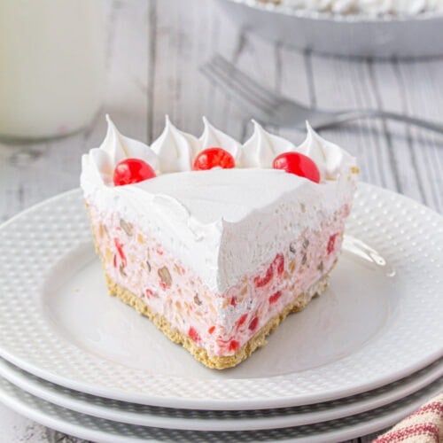 Closeup of a slice of pink cream pie with cherries on top on a white plate.