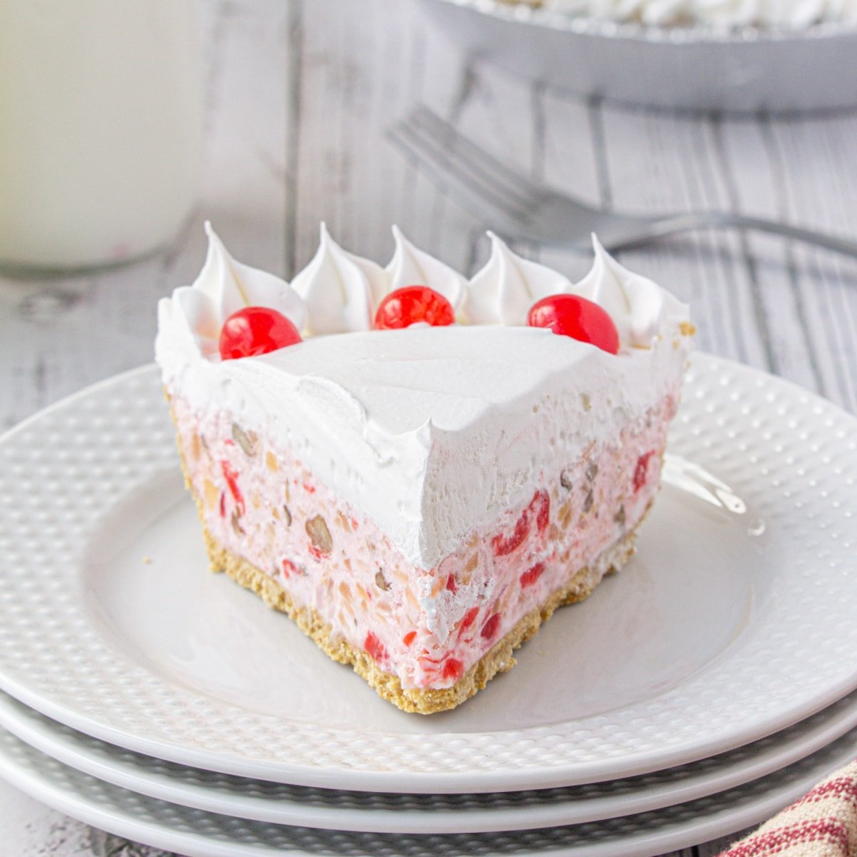 Closeup of a slice of pink cream pie with cherries on top on a white plate.