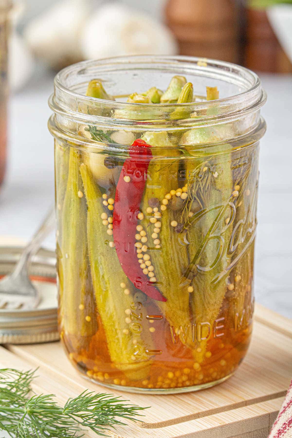 Pickled okra in a canning jar with a red chile.