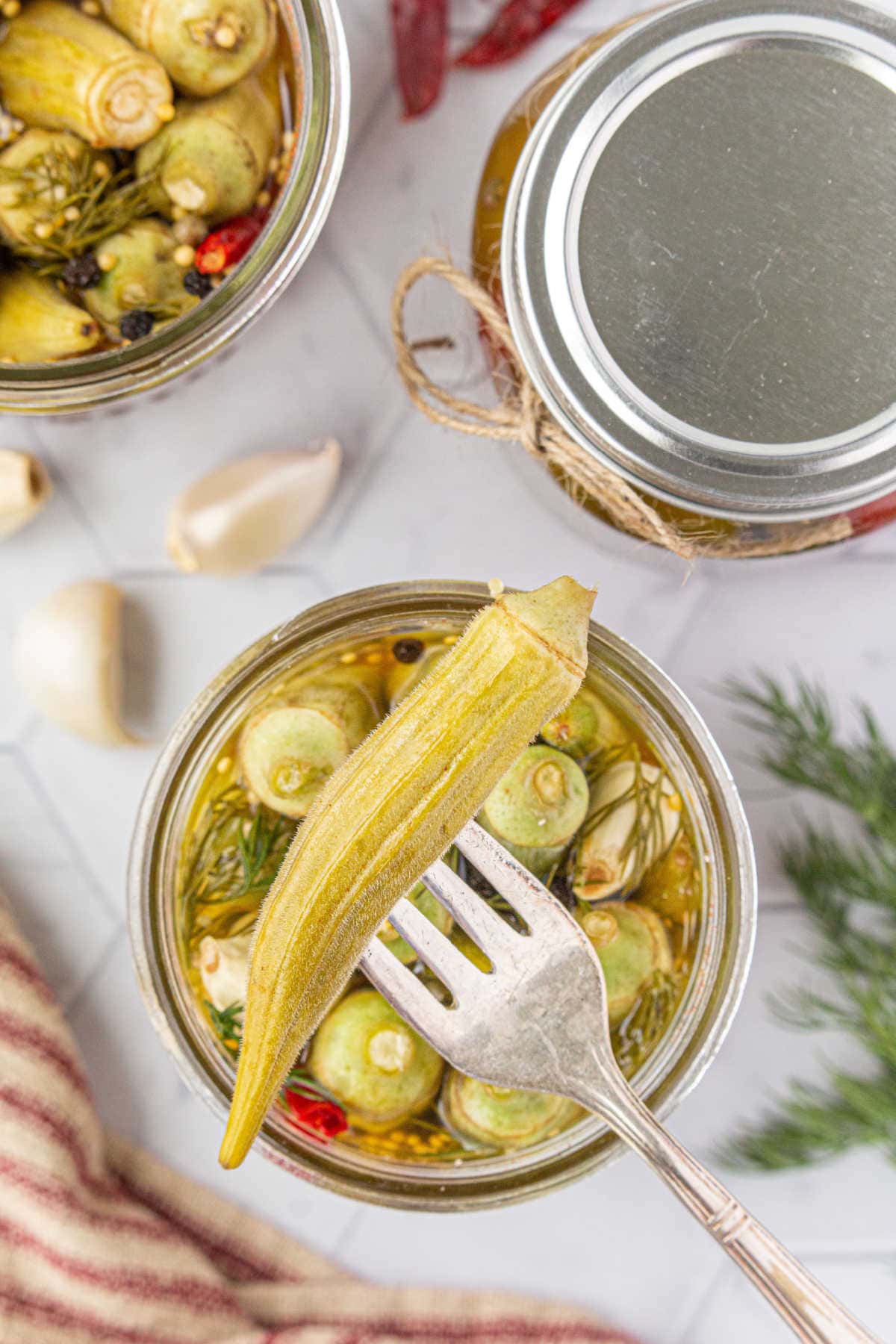 A fork spearing s pod of pickled okra out of the jar.