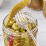 A jar of finished okra pickles on a table with text overlay for Pinterest.