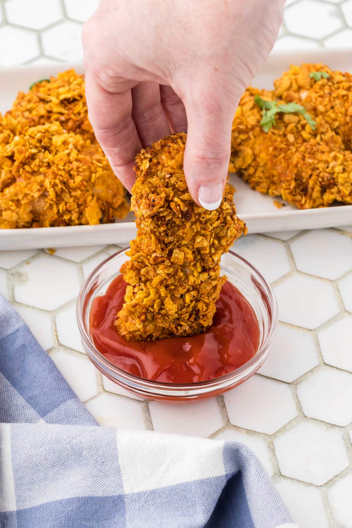 A crispy chicken tender being dipped in ketchup.