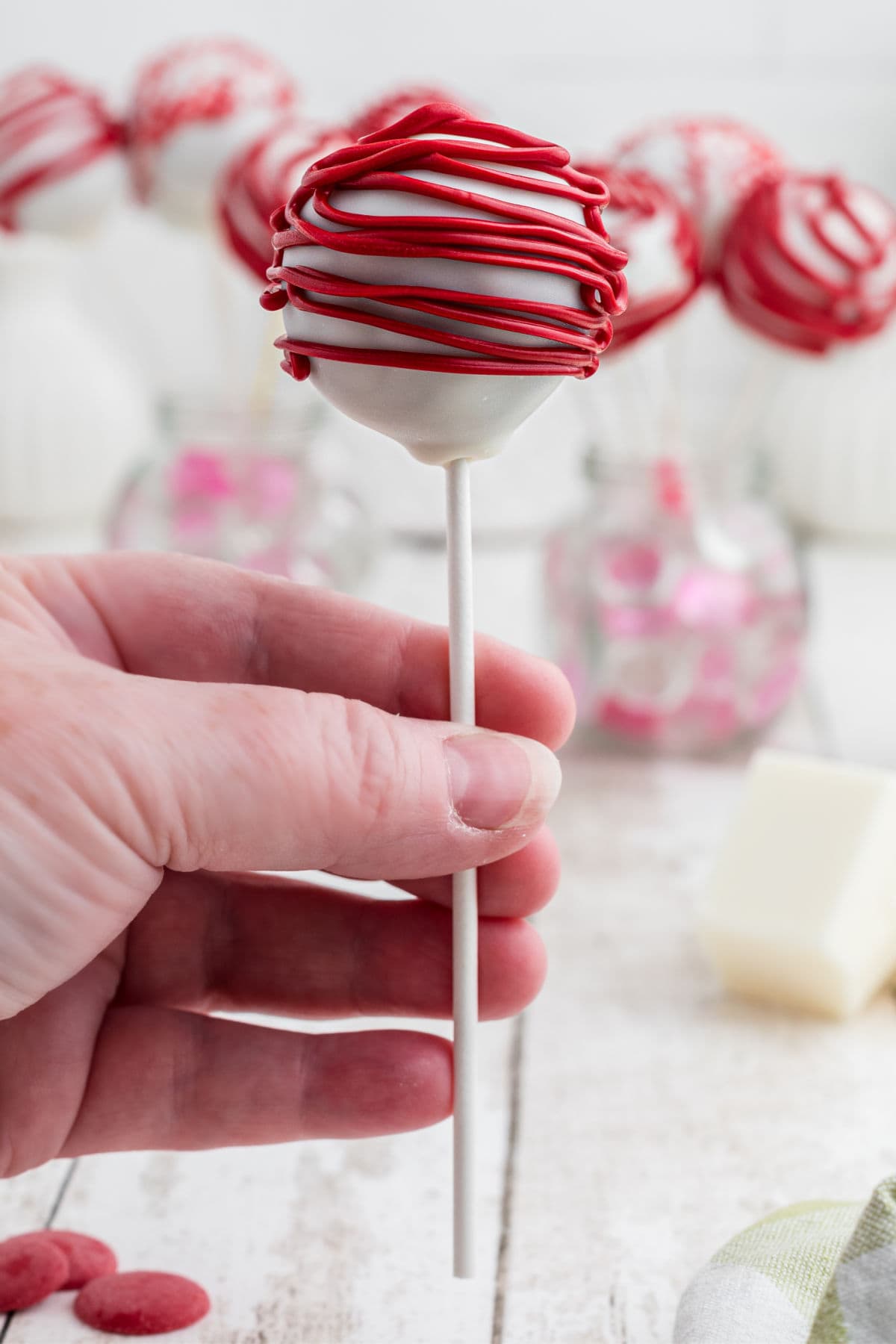 A hand holding a decorated red velvet cake pop.