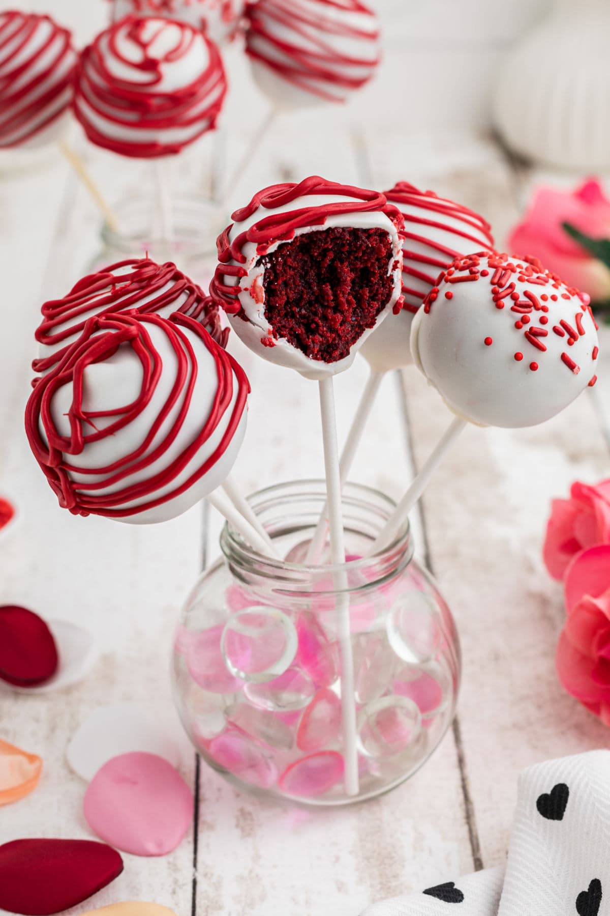 A group of cake pops in a jar with one opened up so you can see the red velvet cake inside.
