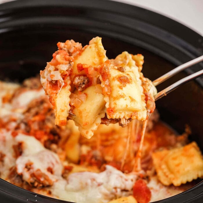 Ravioli in sauce being spooned out of a crockpot.