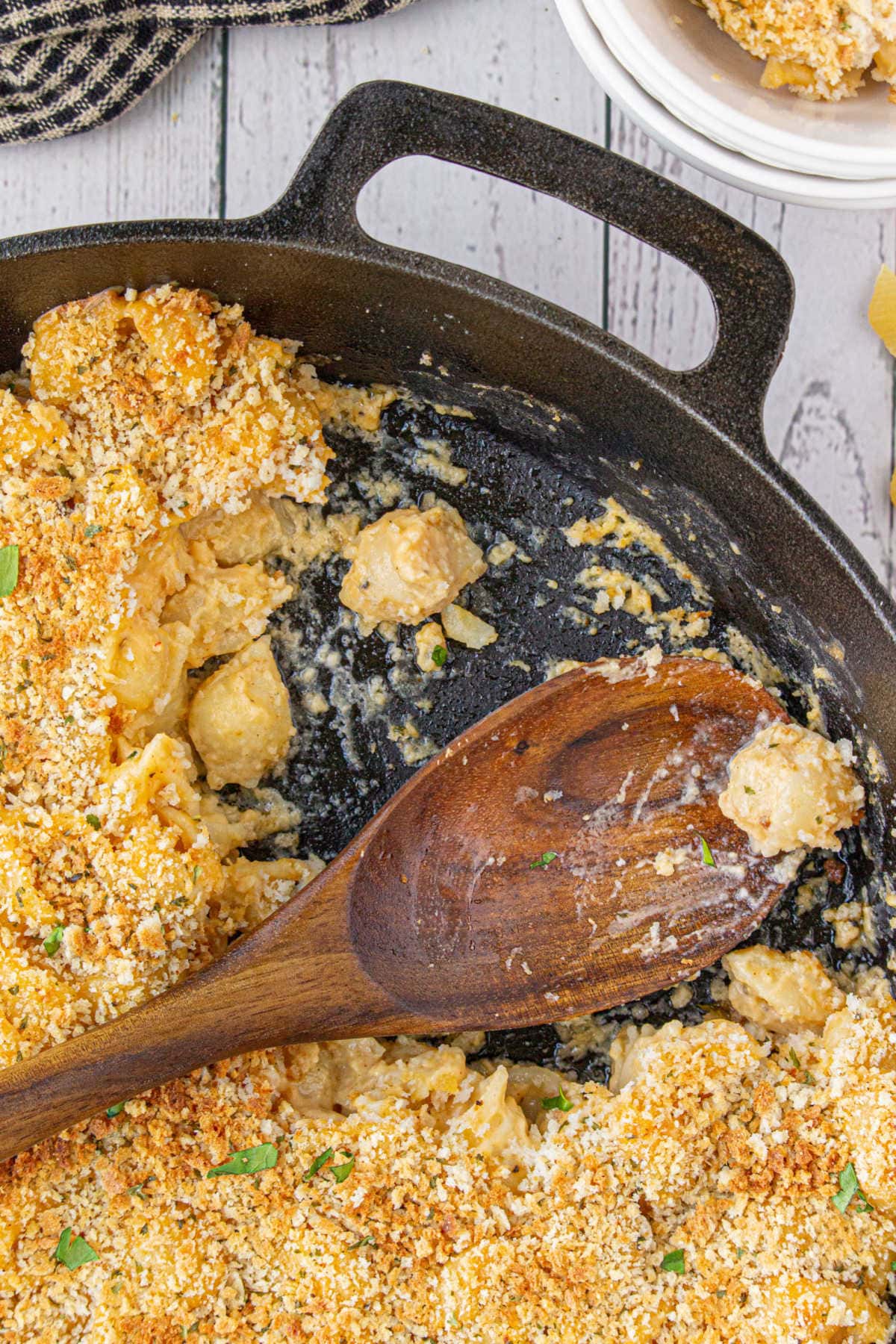 A wooden serving spoon in a skillet of creamy mac and cheese.