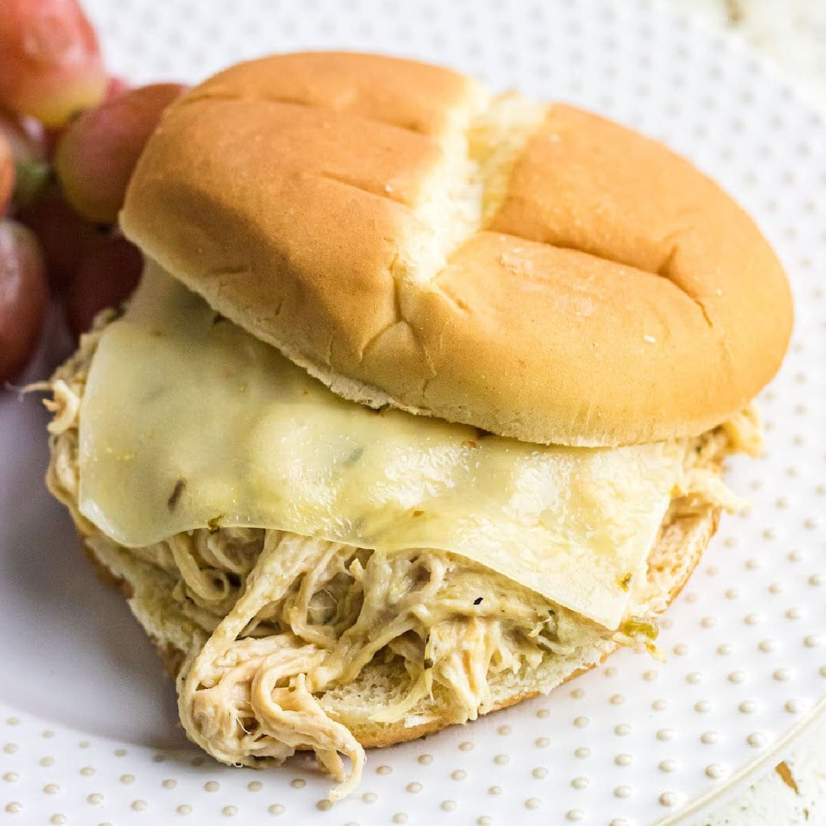 A shredded chicken sandwich on a white plate.