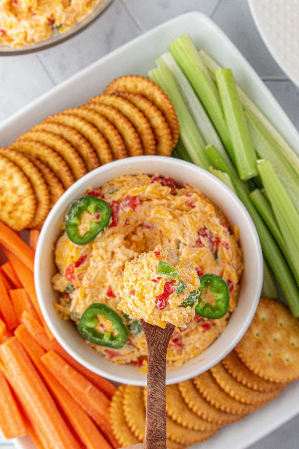Overhead view of a bowl of pimento cheese surrounded by crackers and veggies.