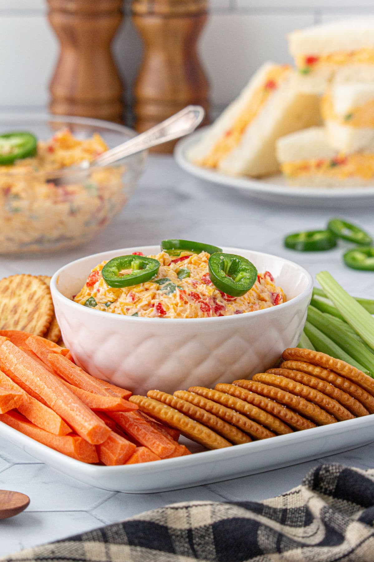 Pimento cheese in a bowl with crackers and sandwiches on plates. Serving suggestion.