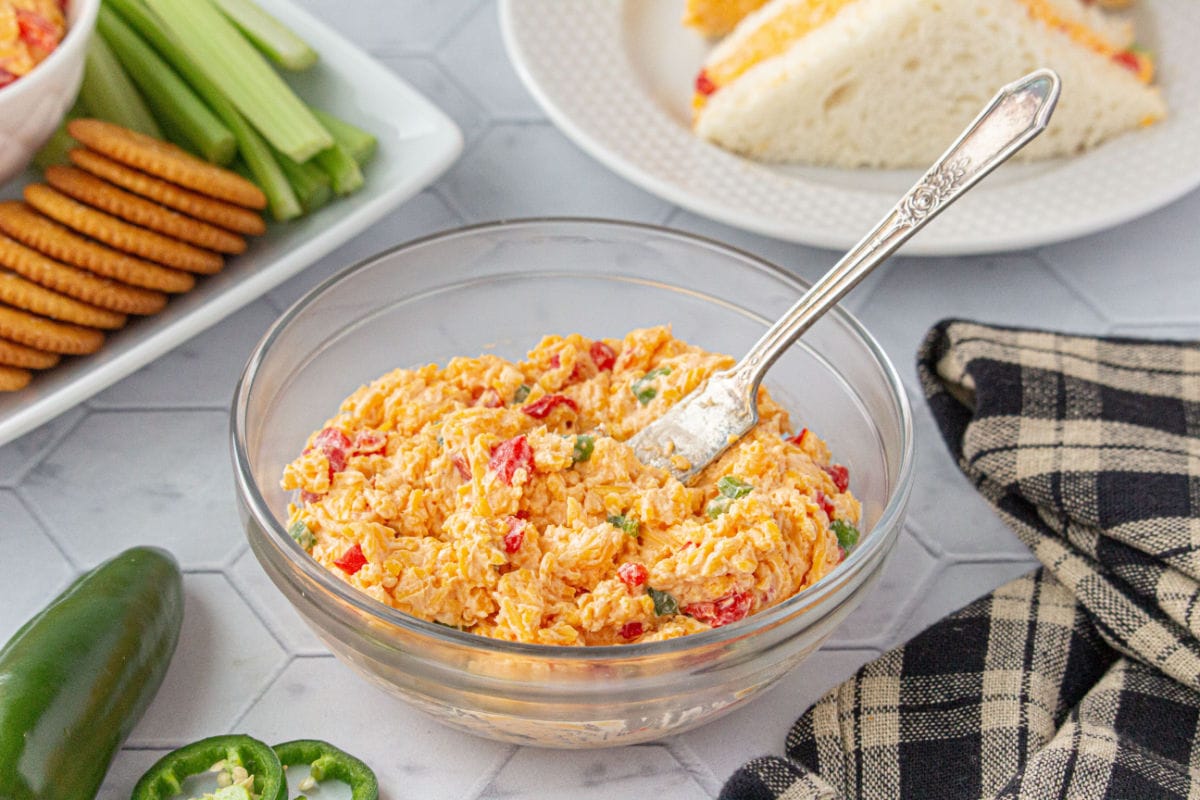 A bowl of pimento cheese on a table with a black and white linen.