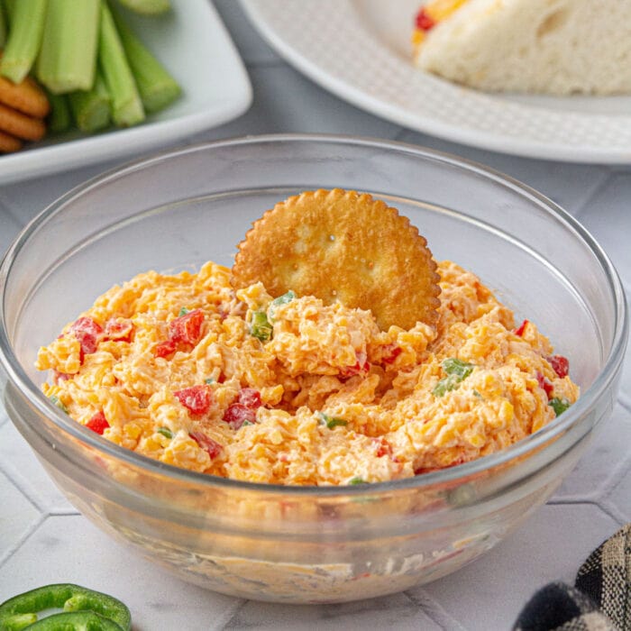 A bowl of pimento cheese spread with a cracker in it.