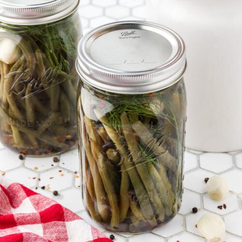 Two jars of pickled green beans with the caps on them.