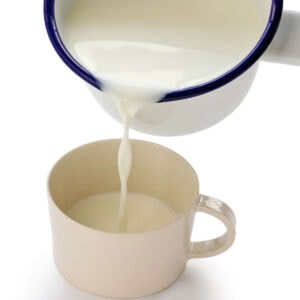 Hot, scalded milk being poured from a pan into a cup.