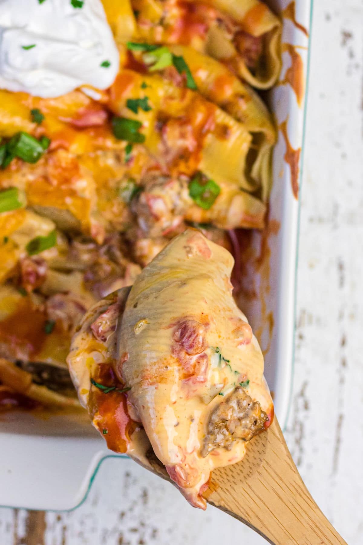 A serving of cheesy taco stuffed shells being lifted from the casserole dish.