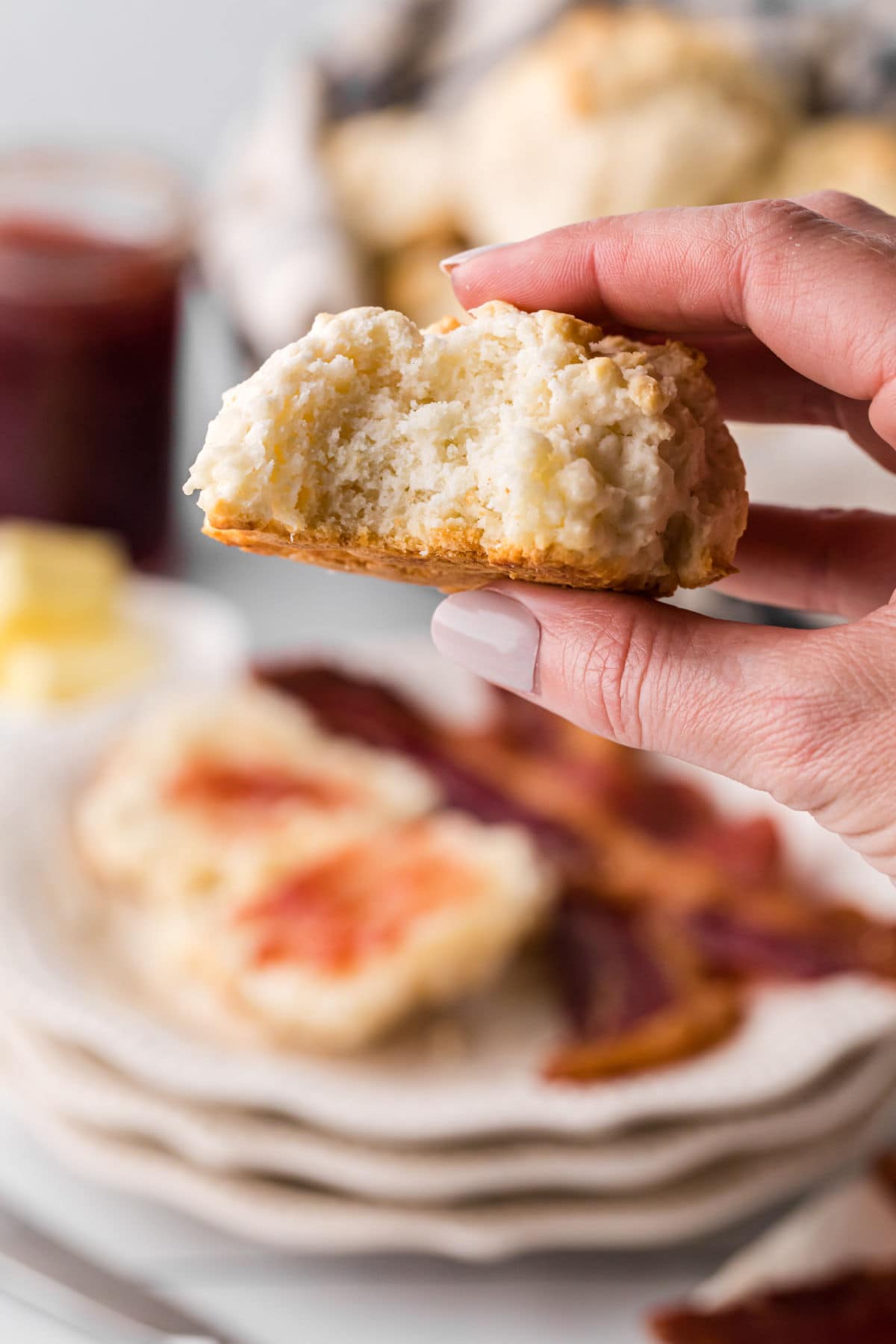 A woman's hand holding a biscuit showing the flaky interior.