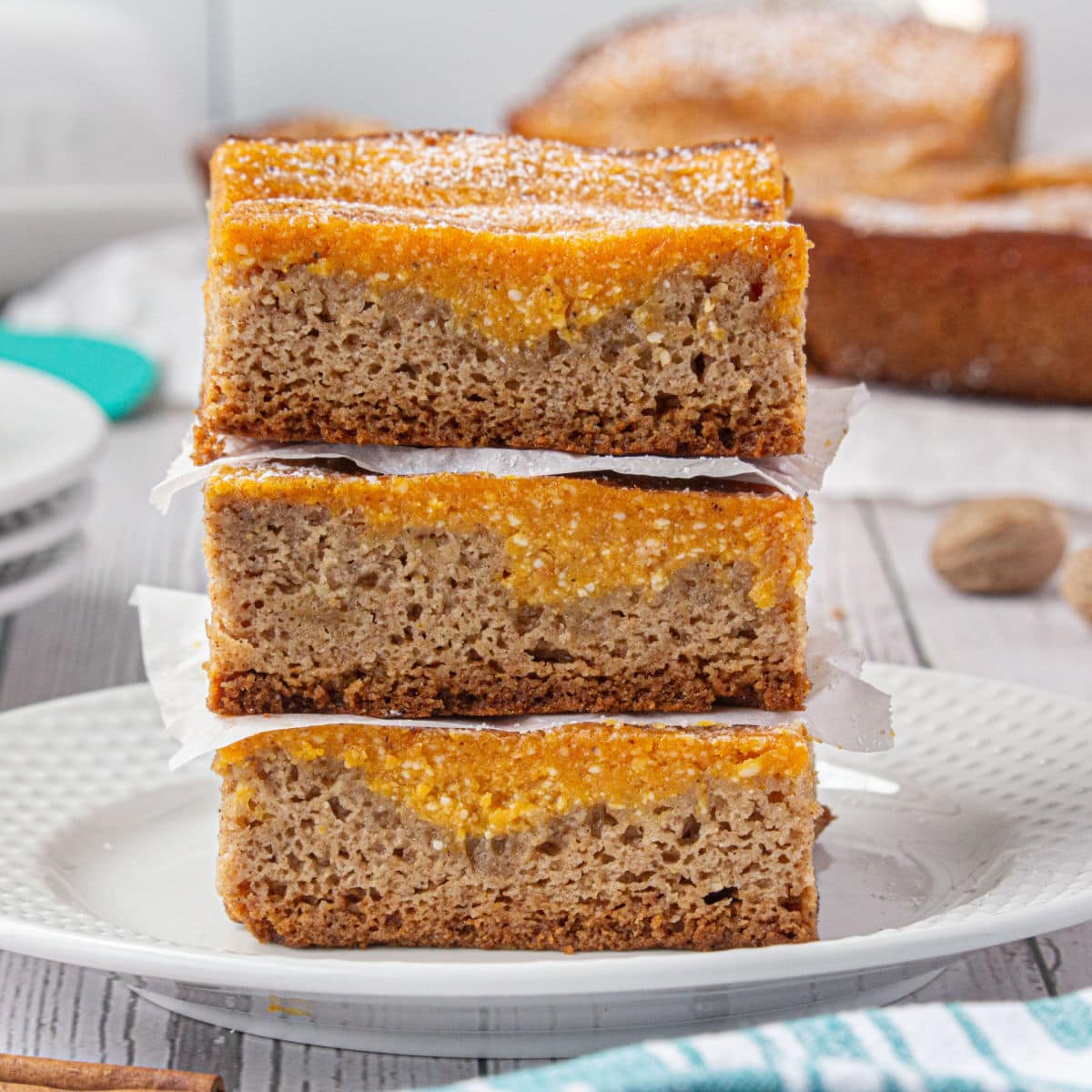 A stack of pumpkin bars on a plate showing the layers of spice cake and pumpkin.