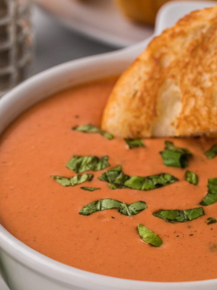 Closeup of a bowl of tomato soup with a grilled cheese sandwich being dipped in it.